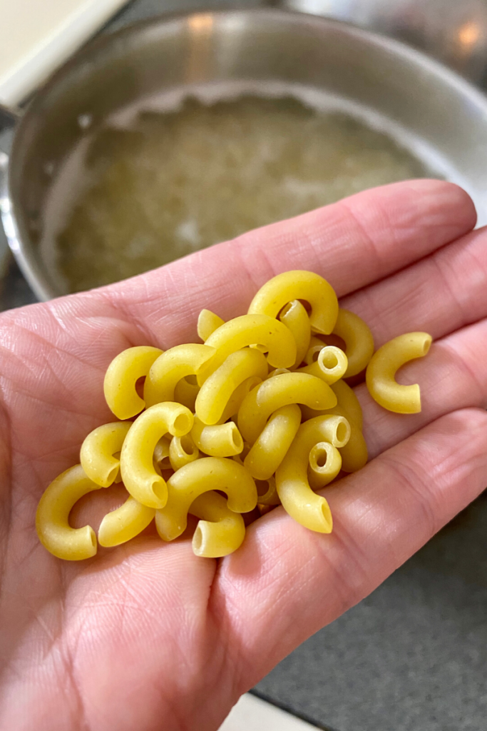 Elbow macaroni in a hand above a pot of hot water