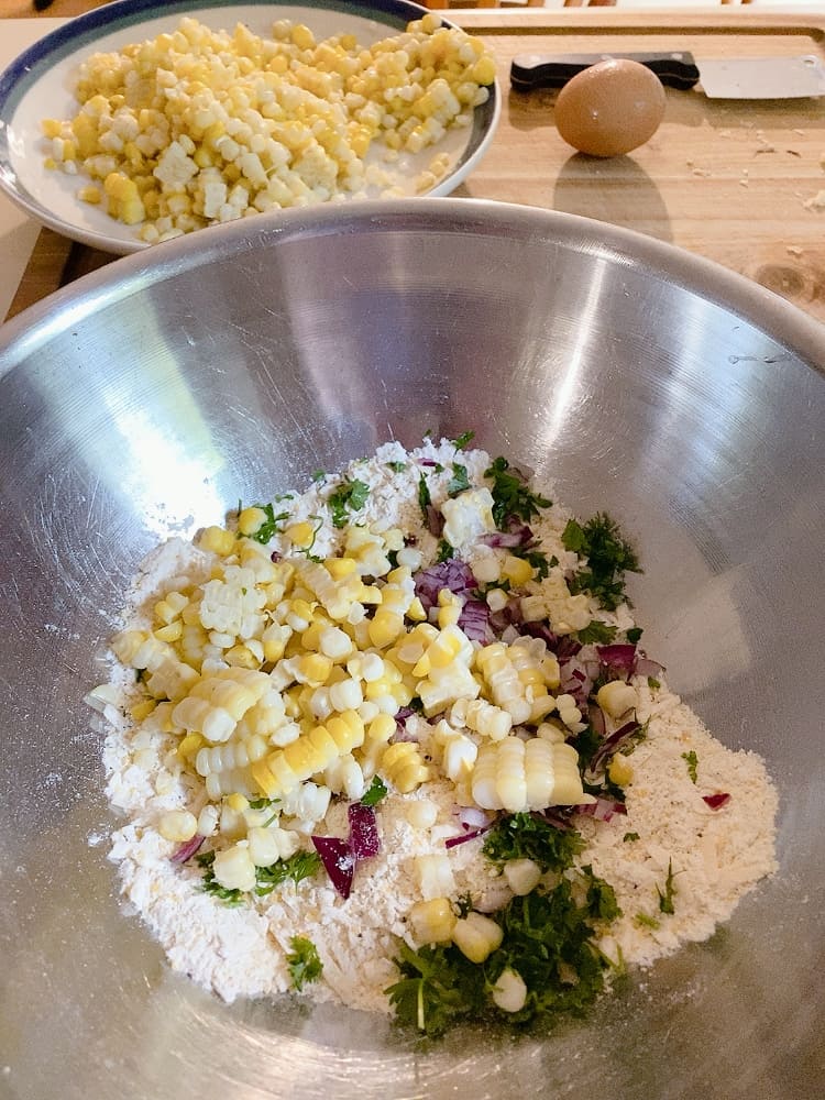 cheesy corn fritters ingredients in a bowl including fresh corn, onion, parsley, flour, corn meal and cheese