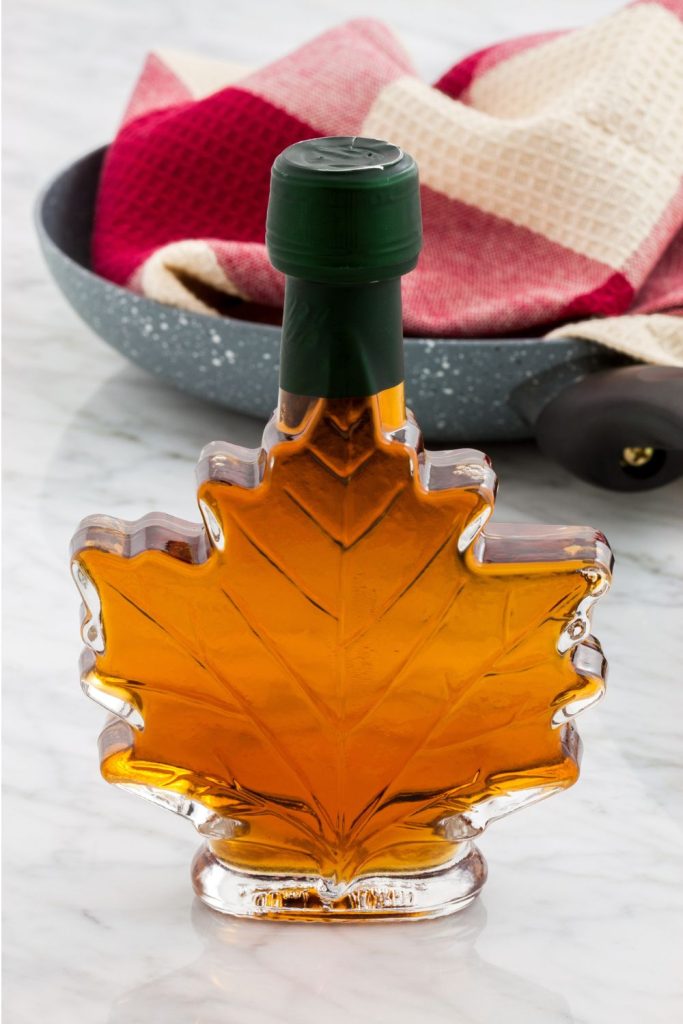 maple syrup in a leaf shaped bottle with plate and towel on table